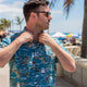Man adjusting vibrant Hawaiian shirt on beach boardwalk