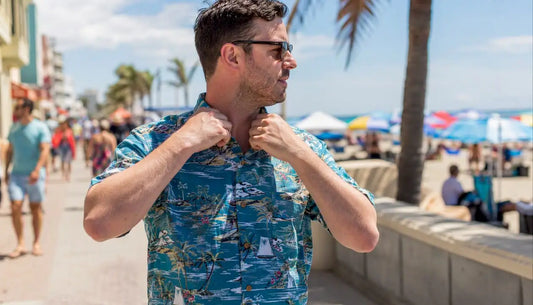 Man adjusting vibrant Hawaiian shirt on beach boardwalk