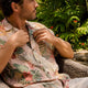 Man buttoning Dan Flashes natural-dyed Hawaiian shirt on patio