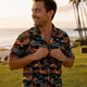 Man buttoning vibrant Hawaiian shirt at sunset beach