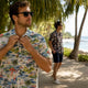Man adjusting rayon Hawaiian shirt on tropical boardwalk