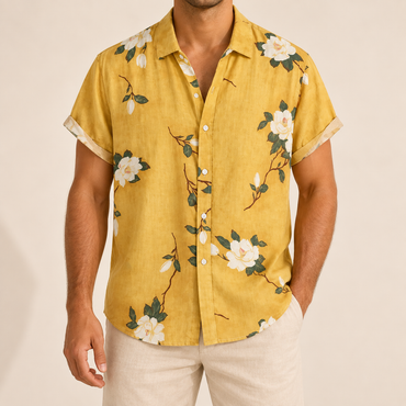 Model wearing yellow short-sleeve Hawaiian shirt with light blossoms and green stems