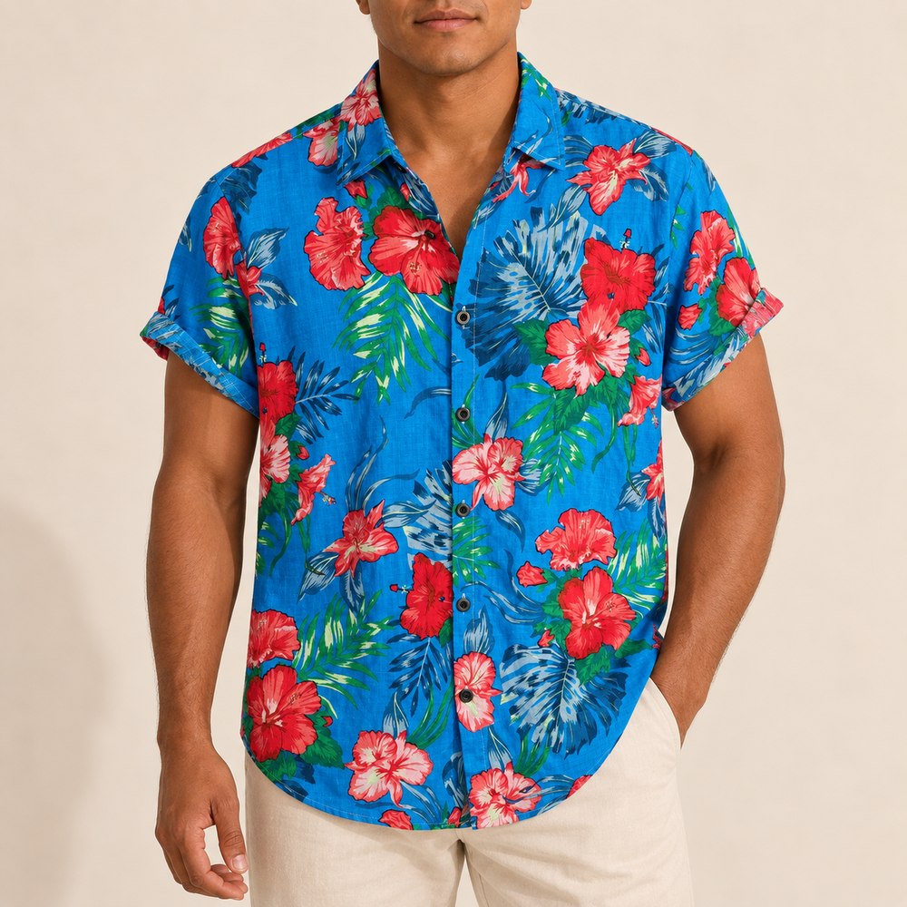 Model wearing blue Hawaiian shirt with red hibiscus-like flowers and green leaves