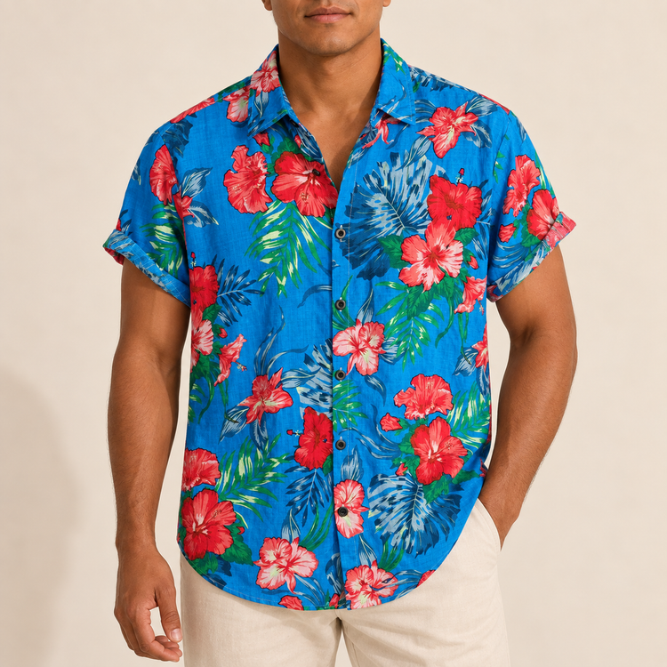 Model wearing blue Hawaiian shirt with red hibiscus-like flowers and green leaves
