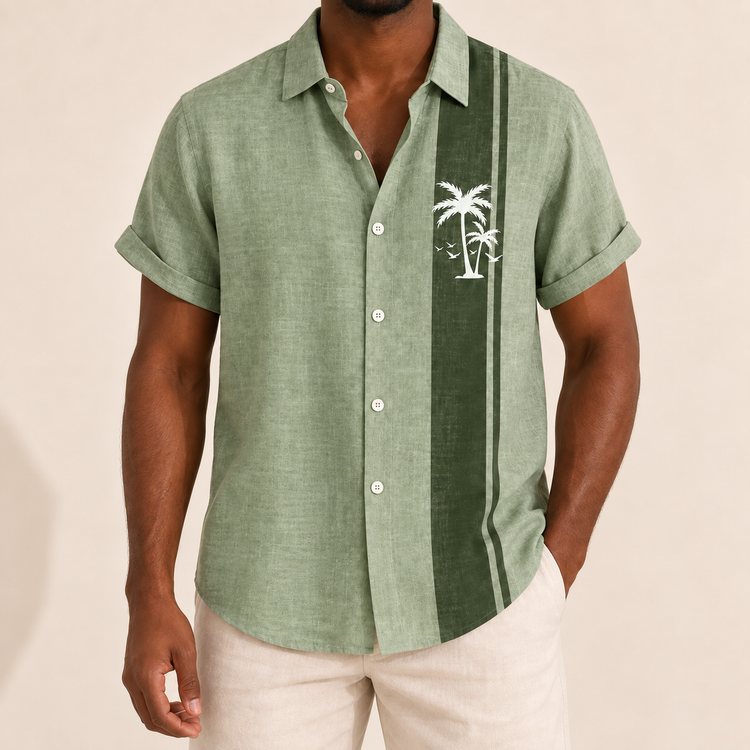 Model wearing sage green short-sleeve shirt with a dark panel and pale palm tree motif