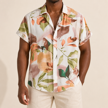 Model wearing a white short-sleeve shirt with soft peach, sage green and brown botanical shapes